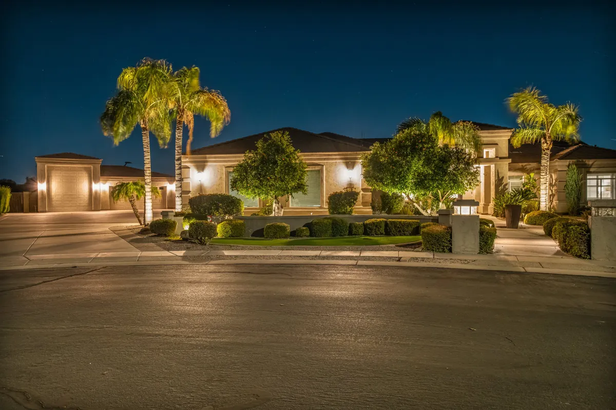 The exterior of the home is illuminated in the evening, with palm trees and a manicured garden leading up to an inviting, well-lit entrance. The spacious yard is perfect for outdoor dining, stargazing, or evening gatherings, with the sunset creating a warm, welcoming atmosphere.