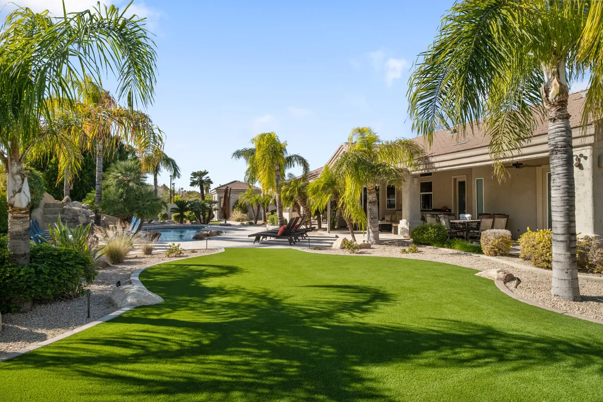 This exterior image captures a lush green lawn, a sparkling swimming pool surrounded by palm trees, and a comfortable outdoor seating area. The wide angle frames the inviting pool as the centerpiece, with the house visible in the background and the sky transitioning into evening, suggesting a place perfect for both active outdoor fun and relaxing gatherings.