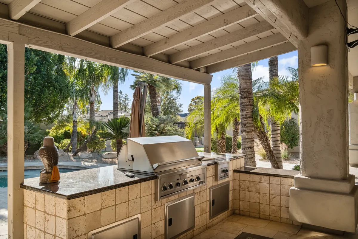 An inviting outdoor grill and entertainment area with a granite countertop, adjacent to a shimmering pool and framed by palm trees. The space is clearly designed for group activities such as barbecues, intimate dinners, and relaxed poolside conversations.
