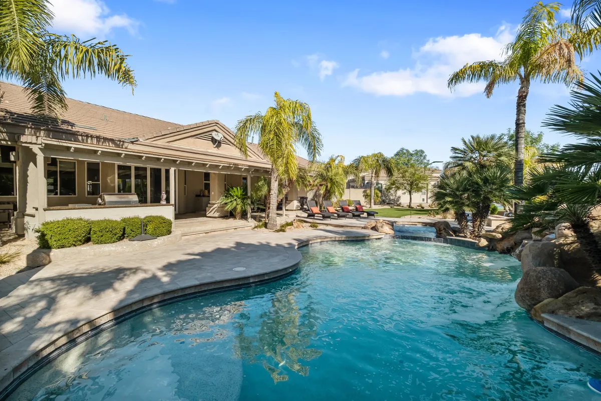 This exterior image showcases the inviting swimming pool surrounded by palm trees, elegant lounge chairs, and the house's exterior. The tranquil setting highlights spaces for sunbathing, swimming, and entertaining guests, with the golden hues of sunset adding a resort-like atmosphere.