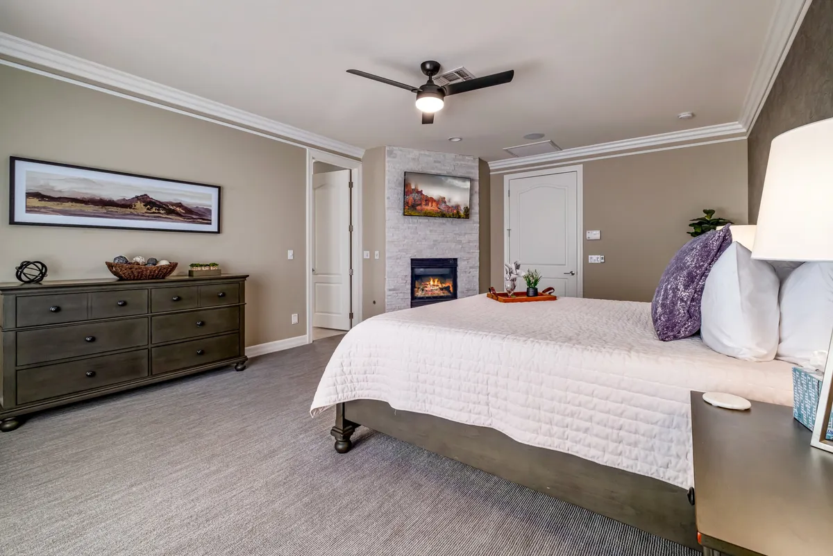 This image showcases a serene bedroom featuring a plush king bed, a cozy fireplace, stylish dresser, and tasteful artwork. The atmosphere is peaceful and inviting, ideal for relaxation and restful sleep.