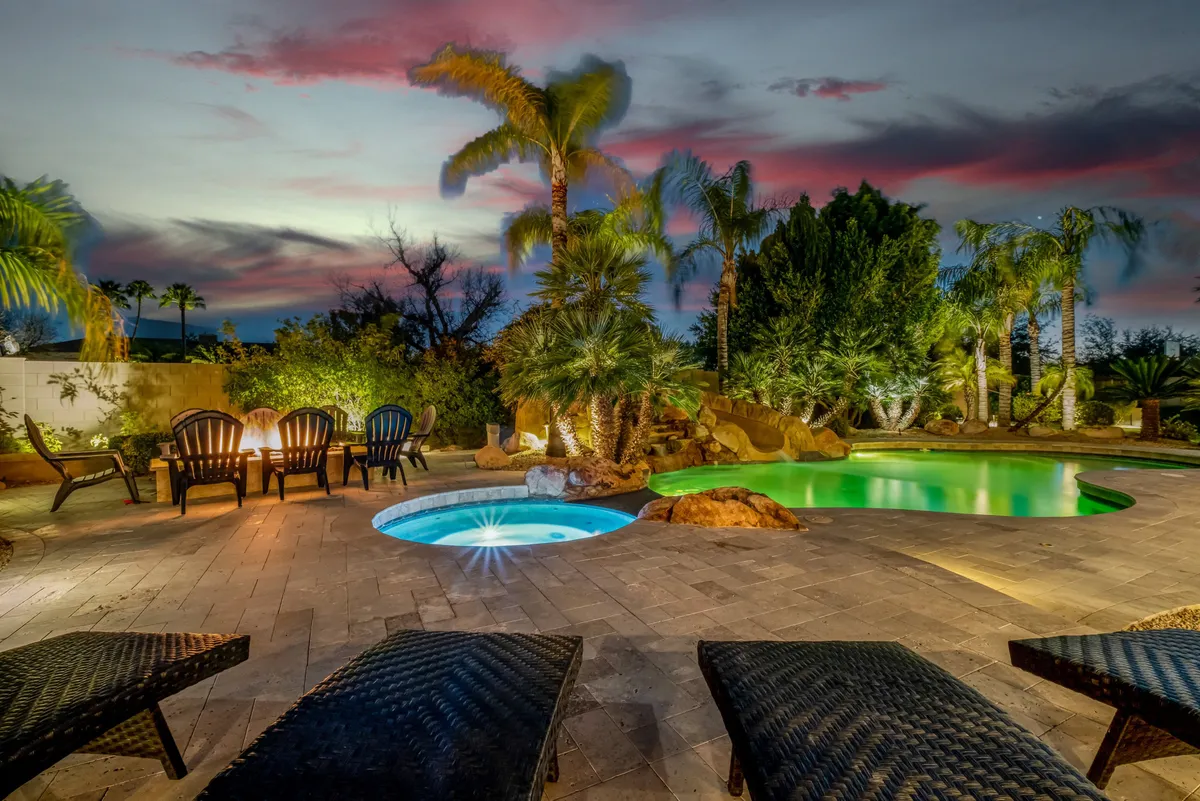 This image displays a lush backyard with a swimming pool, hot tub, outdoor seating area, palm trees, and well-maintained landscaped garden. The inviting arrangement highlights spaces ideal for relaxation and social gatherings after a day of golf.