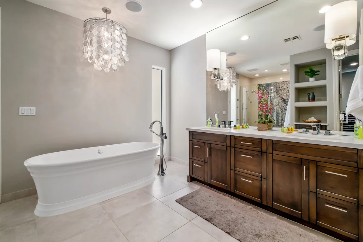 A sophisticated bathroom scene displaying a freestanding bathtub, dual-sink vanity, elegant chandelier, and lush greenery. The design is luxurious, echoing a spa-like experience.