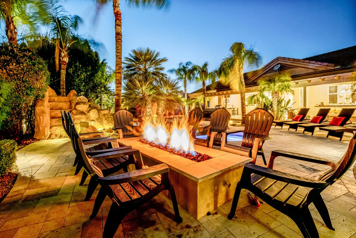 A cozy fire pit surrounded by comfortable chairs, framed by palm trees and a landscaped backyard. The image evokes the warmth and camaraderie of gathering outdoors in the evening.