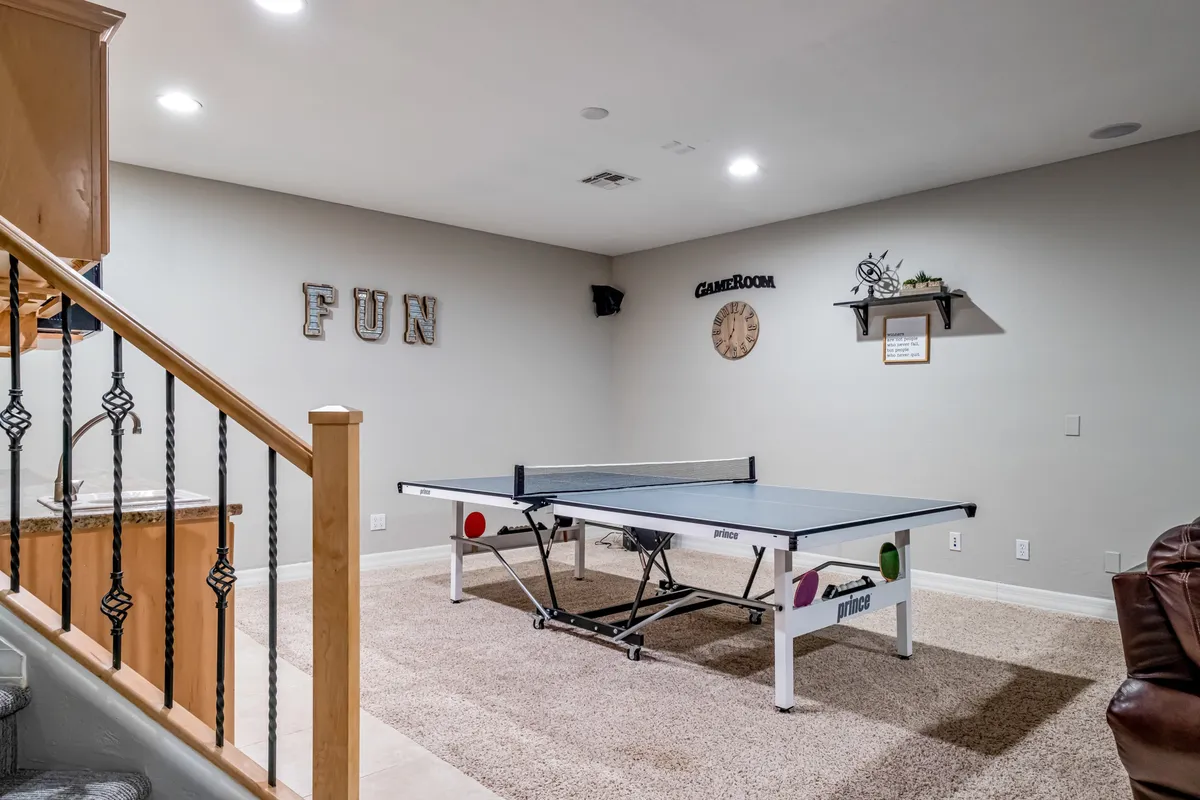 An interior shot highlighting a ping pong table set against a decorative wall, with a staircase leading to other areas. The atmosphere is energetic and social, ideal for friendly competitions or group gatherings.