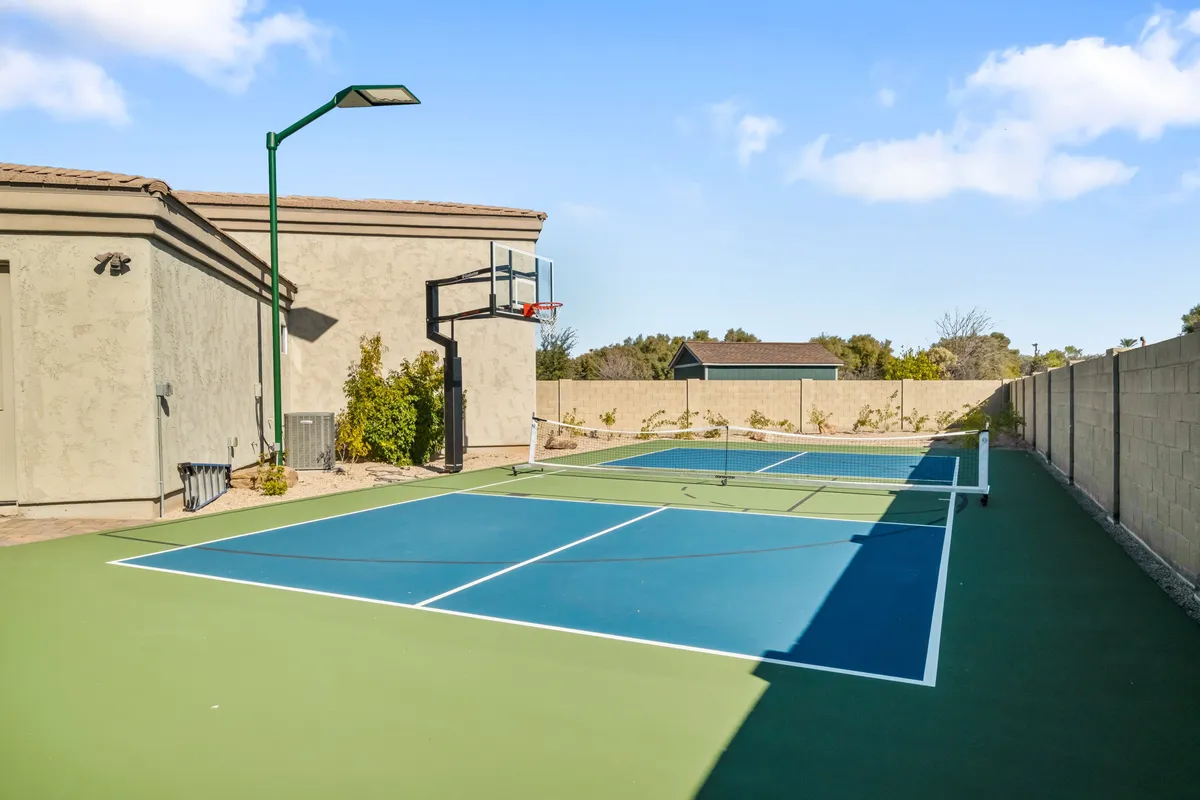 A vibrant sports area featuring a tennis court and a basketball hoop, surrounded by greenery. The court is ready for friendly pickleball or basketball matches, adding a spirited, energetic dimension to the backyard retreat.