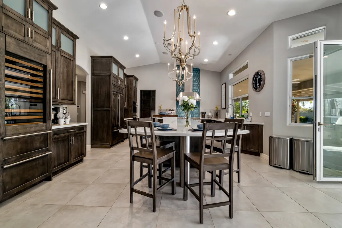 A beautifully set dining table sits beneath a striking chandelier, surrounded by modern cabinetry and elegant decor. The space is designed for hosting large groups, making it ideal for celebratory meals and family feasts.