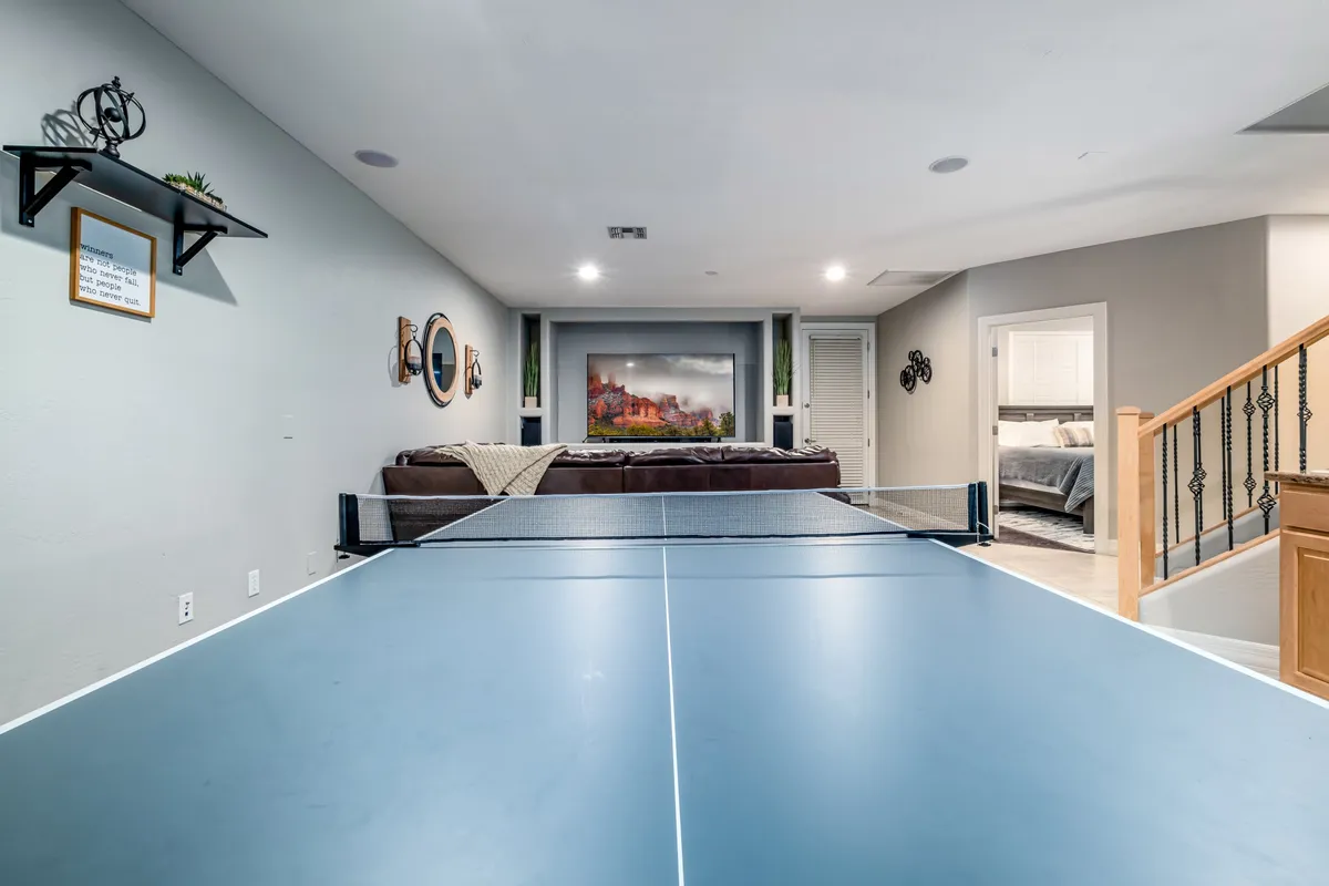 A lively interior game room with a ping pong table as the centerpiece, a sofa for relaxing, stylish wall art, and a shelving unit for games and books. The space is bright and inviting, designed for both active play and casual hangouts.