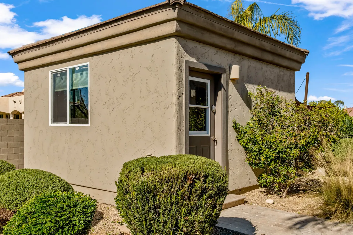 This exterior shot features a small, standalone building nestled within landscaped bushes and a welcoming pathway. The scene conveys privacy and versatility—ideal for highlighting the separate backyard casita with its own en suite bath, mentioned as a perfect option for in-laws or friends.