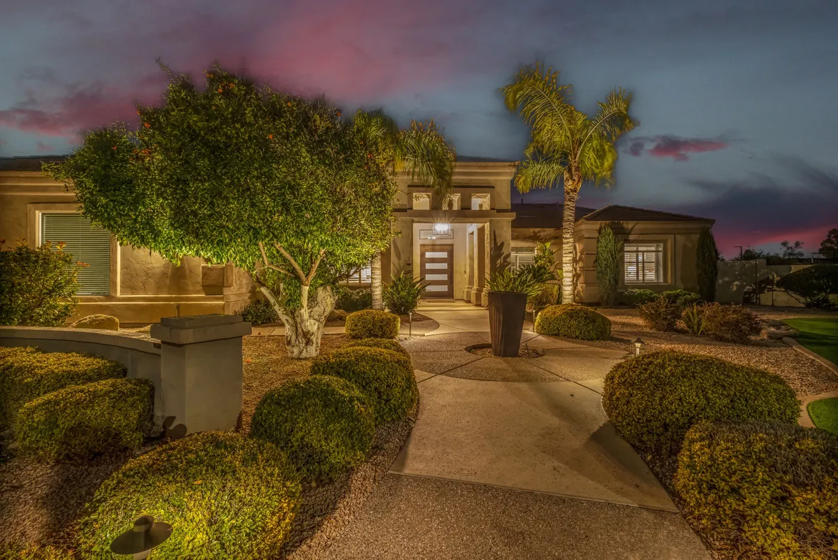 An inviting exterior view of the home's entrance flanked by neatly trimmed bushes and a modern artistic planter. The tranquil, sunlit pathway suggests a warm welcome and the exclusivity of a private villa.